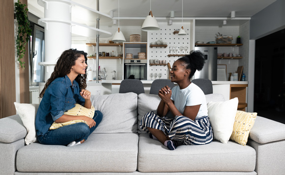two young woman on grey sofa chatting and smiling